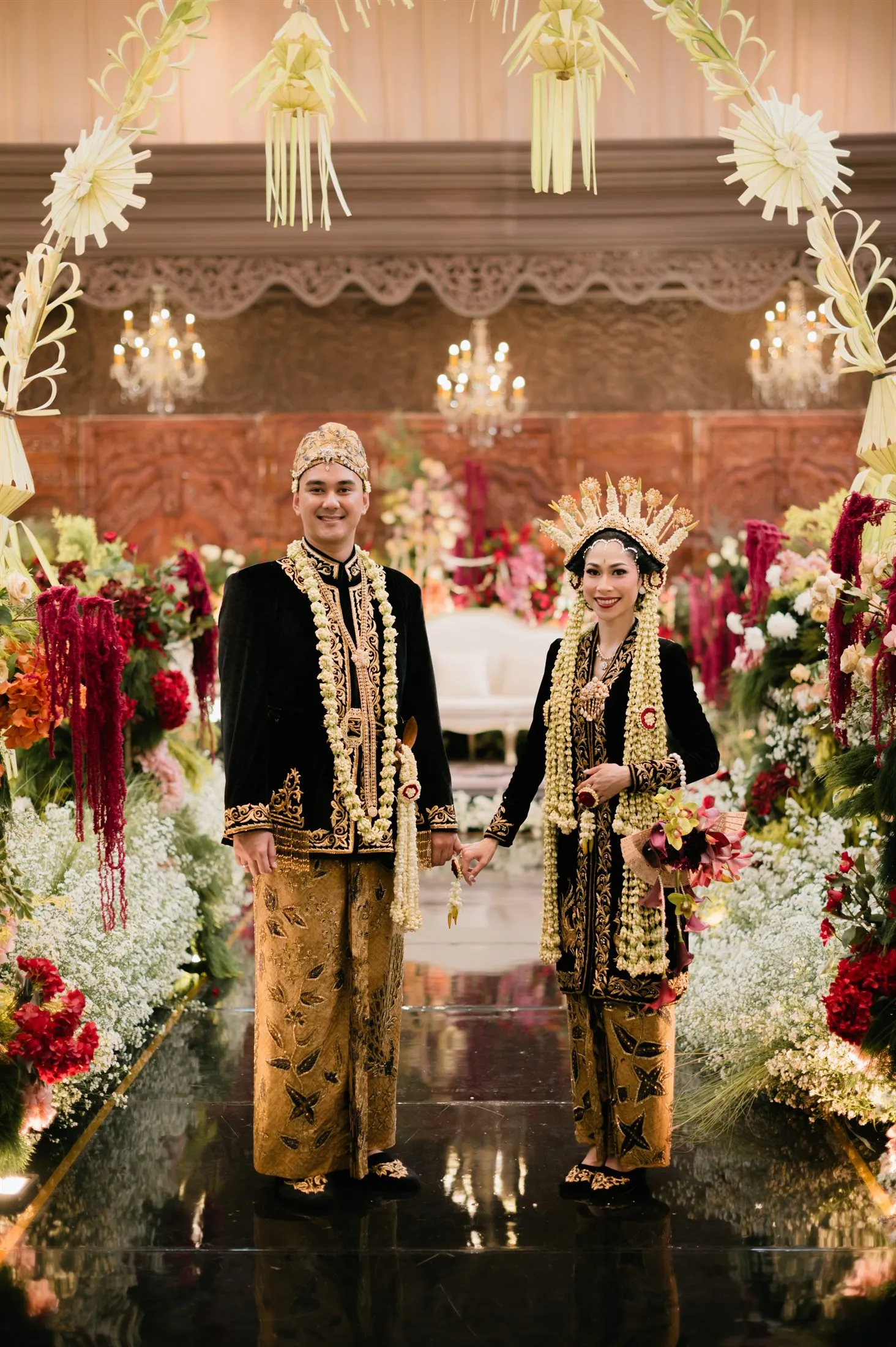 Pasangan pengantin Devano dan Galista berbusana adat Jawa hitam emas di pelaminan resepsi